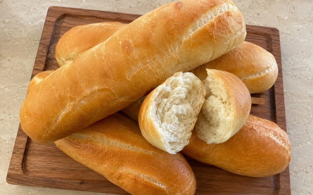 Long French rolls showing smooth golden tops with a single lengthwise slash, on marble surface