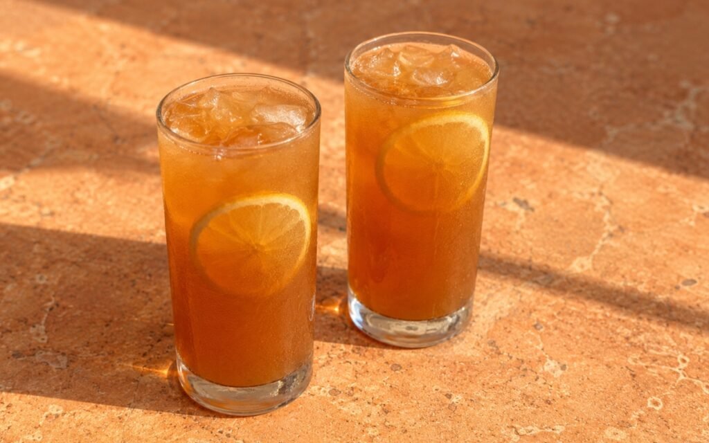 glasses of deep amber tamarind lemonade with lemon wheels floating in ice, on marble surface