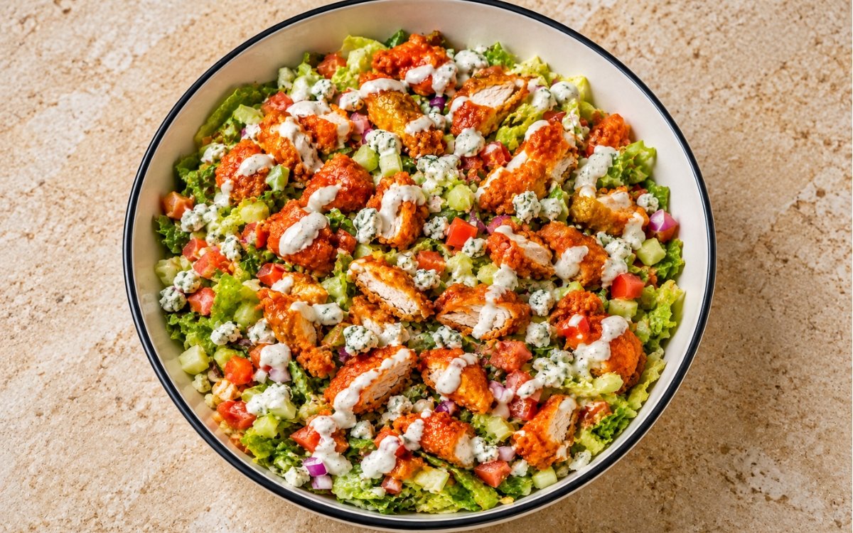 Buffalo chicken chopped salad showing crispy Buffalo chicken pieces over chopped lettuce with celery, tomato, blue cheese, and ranch, on marble surface