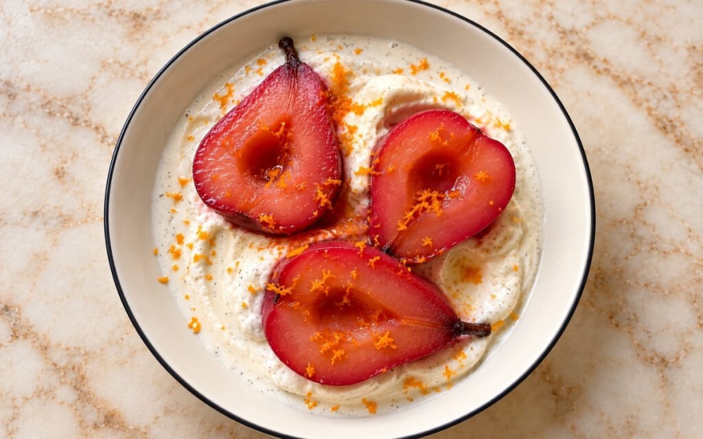 Hibiscus and orange poached pears showing glossy magenta pear halves over vanilla bean ice cream with fresh orange zest, on marble surface