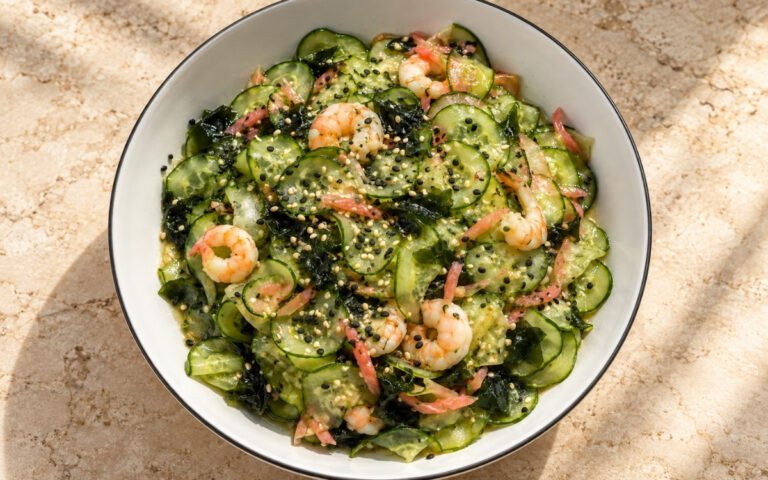 Sunomono showing thinly sliced cucumber, wakame, and shrimp tossed in rice vinegar dressing with sesame seeds and pickled ginger, on marble surface