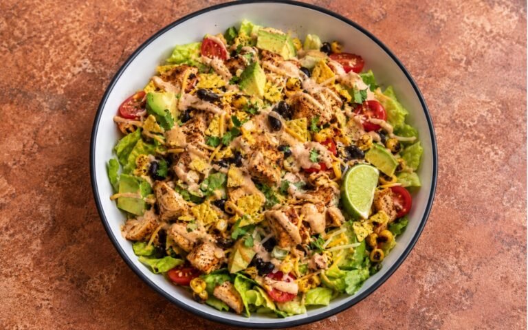 Mexican chicken taco salad showing seasoned chicken, black beans, charred corn, avocado, and crushed tortilla chips with chipotle crema, on marble surface