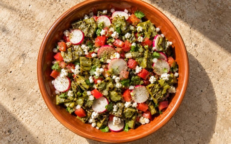 Mexican nopales salad showing diced lightly charred cactus paddles with tomato, radish, cilantro, and crumbled queso fresco, on marble surface