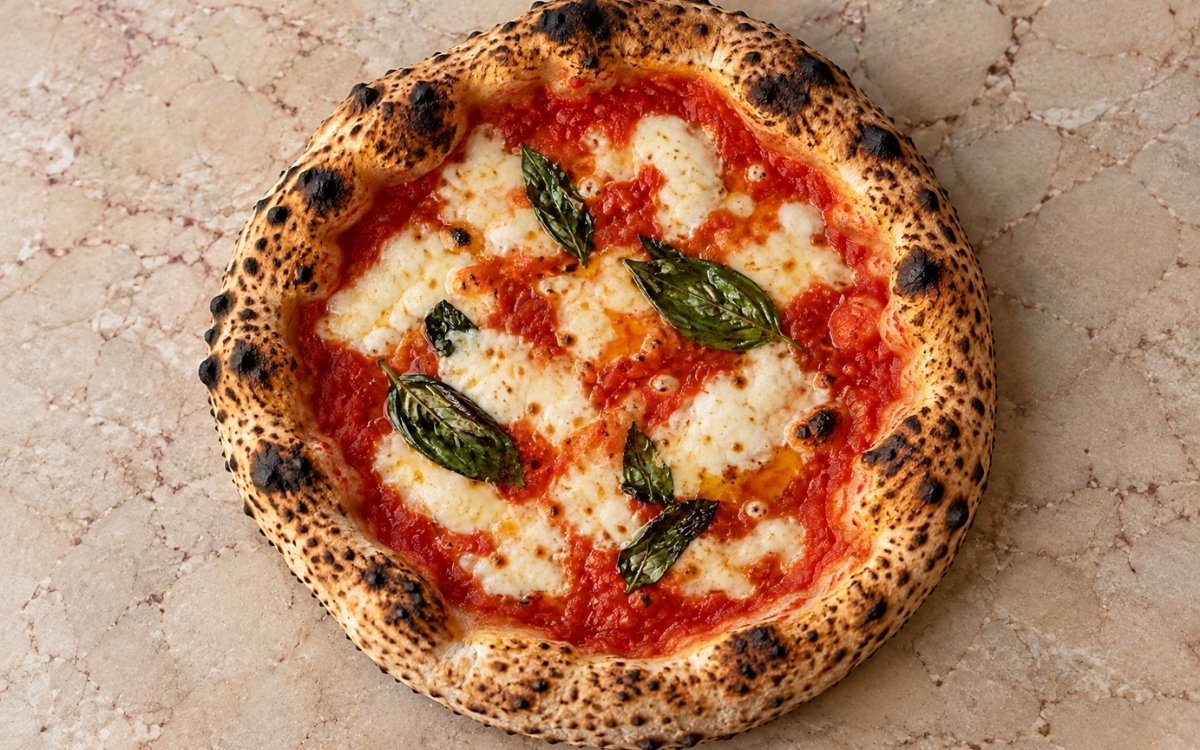 Neapolitan-style Margherita pizza showing a puffed, leopard-spotted crust with melted mozzarella, tomato sauce, and fresh basil, on marble surface