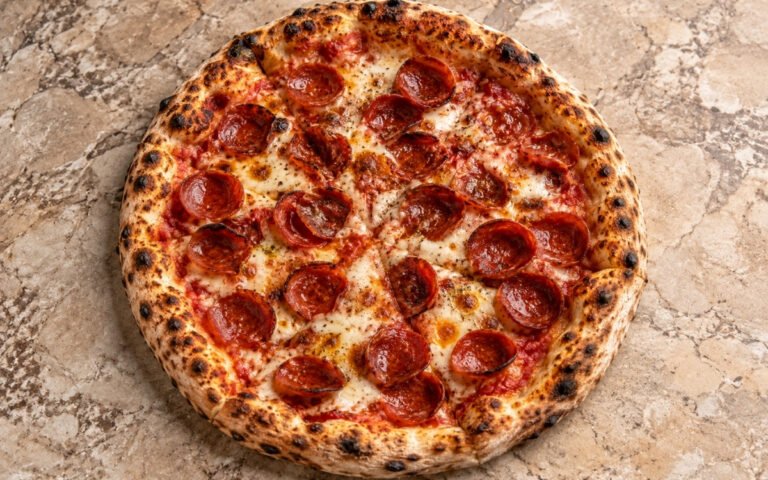Pepperoni pizza showing a golden blistered crust with bubbling mozzarella and crisp curled pepperoni cups, on marble surface