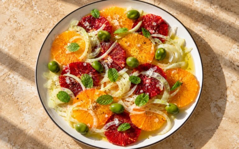 Sicilian orange and fennel salad showing overlapping orange rounds, thinly shaved fennel, olives, and fresh mint, on marble surface