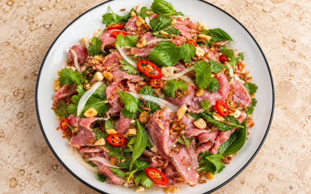 Bò tái chanh showing thinly sliced pink lime-cured beef tossed with fresh herbs, crushed peanuts, and crispy fried shallots, on marble surface