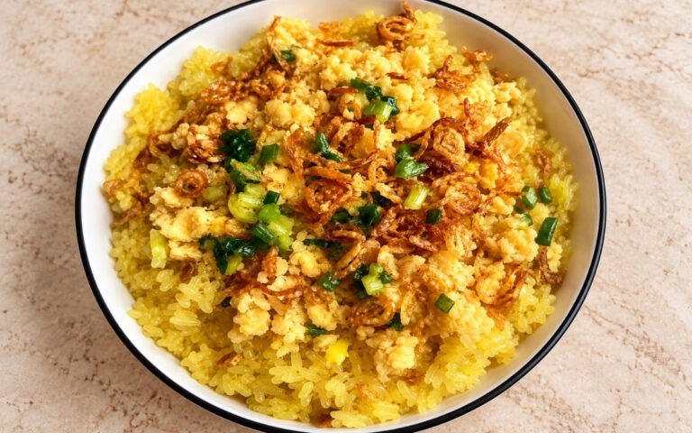 Vietnamese turmeric sticky rice (xôi xéo) showing golden glossy rice topped with crumbled mung bean, crispy fried shallots, and scallion oil, on marble surface