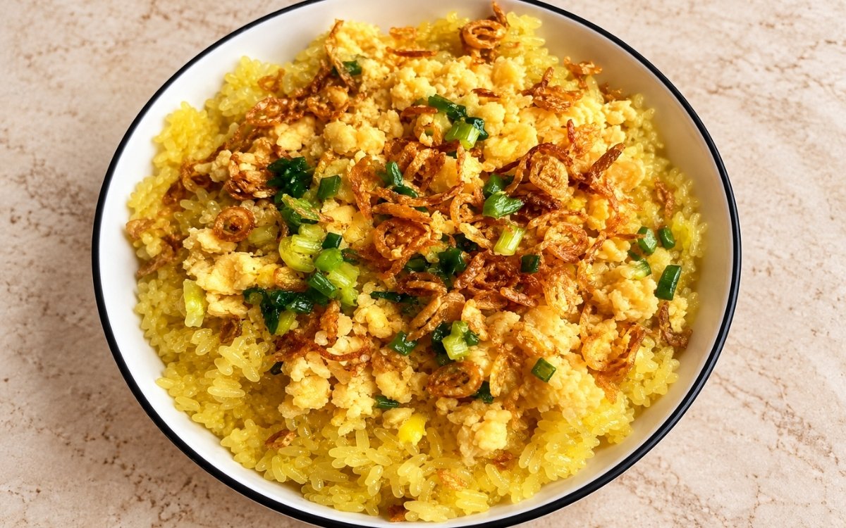 Vietnamese turmeric sticky rice (xôi xéo) showing golden glossy rice topped with crumbled mung bean, crispy fried shallots, and scallion oil, on marble surface