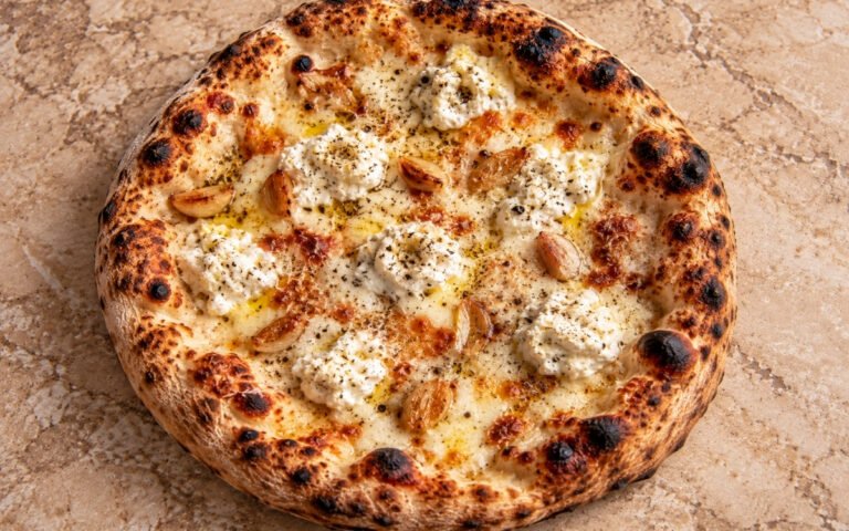 White pizza with ricotta and garlic showing melted mozzarella, soft ricotta dollops, and caramelized garlic over a blistered crust, on marble surface