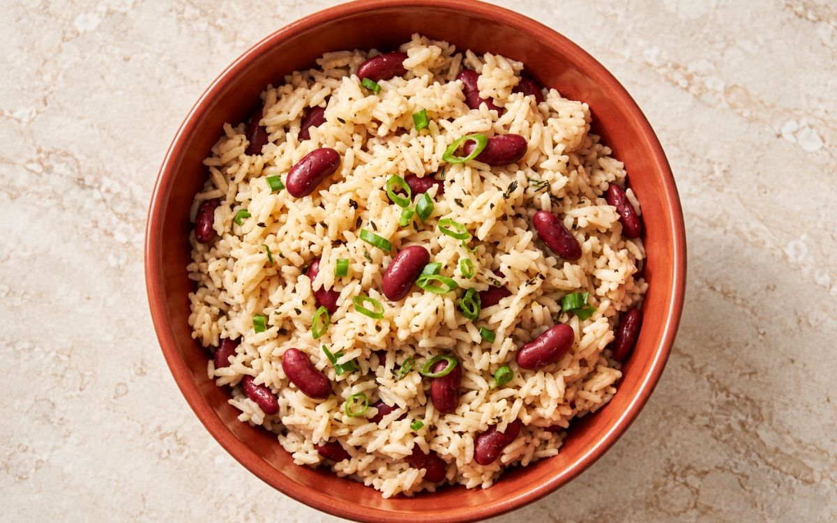 Caribbean coconut rice and beans showing fluffy ivory rice with whole red kidney beans, thyme, and sliced green scallion tops, on marble surface