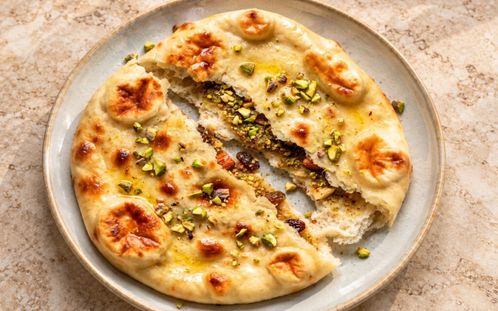 Peshwari naan with golden blistered crust, split open to show the sweet coconut-almond filling