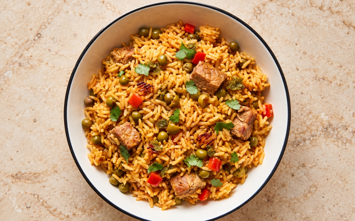 Puerto Rican arroz con gandules showing golden-orange rice with pigeon peas, green olives, red bell pepper, small browned pork cubes, and cilantro, on marble surface